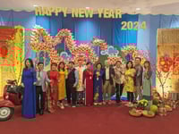 A row of people in colorful dress stand in front of equally colorful decorations and the words "Happy New Year 2024."